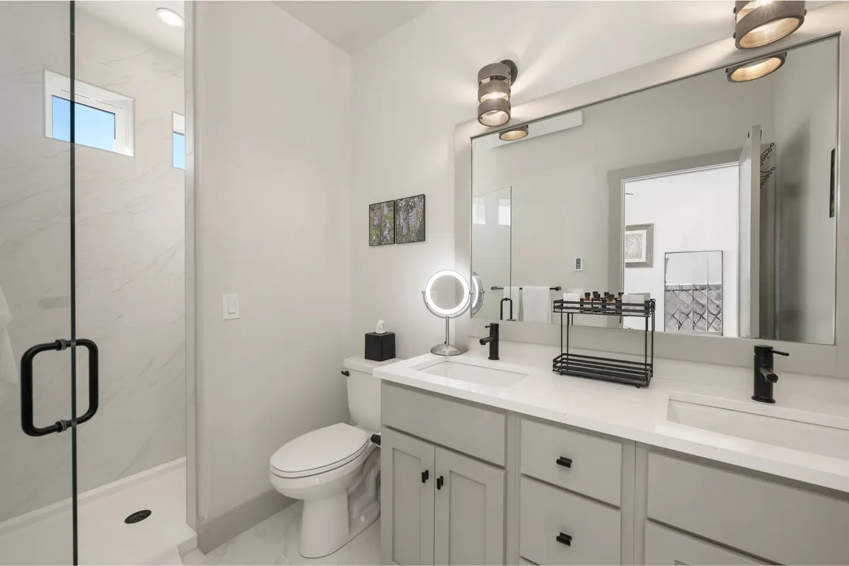 A sleek modern bathroom with a double vanity, stylish sinks, a spacious shower area, and decorative touches. Large mirrors and calming colors enhance the tranquil, spa-like mood of the space.