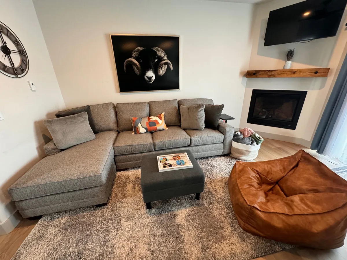A spacious, comfortable living area featuring a sectional sofa, a striking ram artwork, a cozy fireplace, and a bean bag chair. The coffee table and abundant seating create a welcoming environment for relaxation or socializing after a day outdoors.