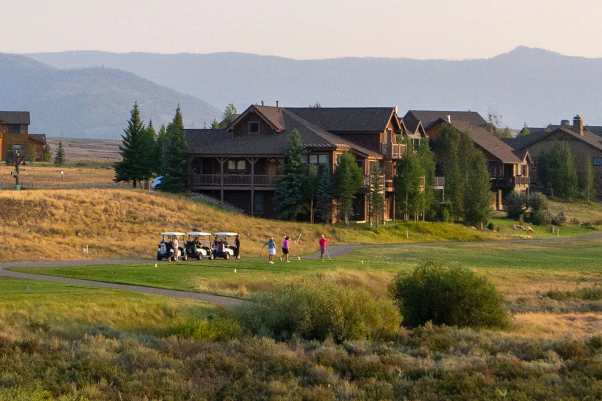 An exterior shot showing golfers enjoying the Grand Elk Golf Course, with scenic mountains and stylish homes in the background. The image captures the sense of community and resort-style leisure activities available to guests.