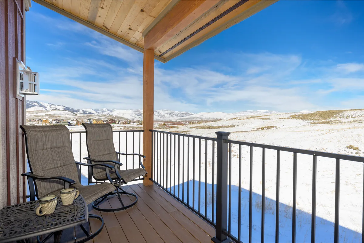 Rocking chairs on a porch overlook a stunning mountain view, with a snow-covered landscape creating a cozy, tranquil atmosphere. The scene suggests relaxation after active days and invites guests to enjoy the natural surroundings from the comfort of home.
