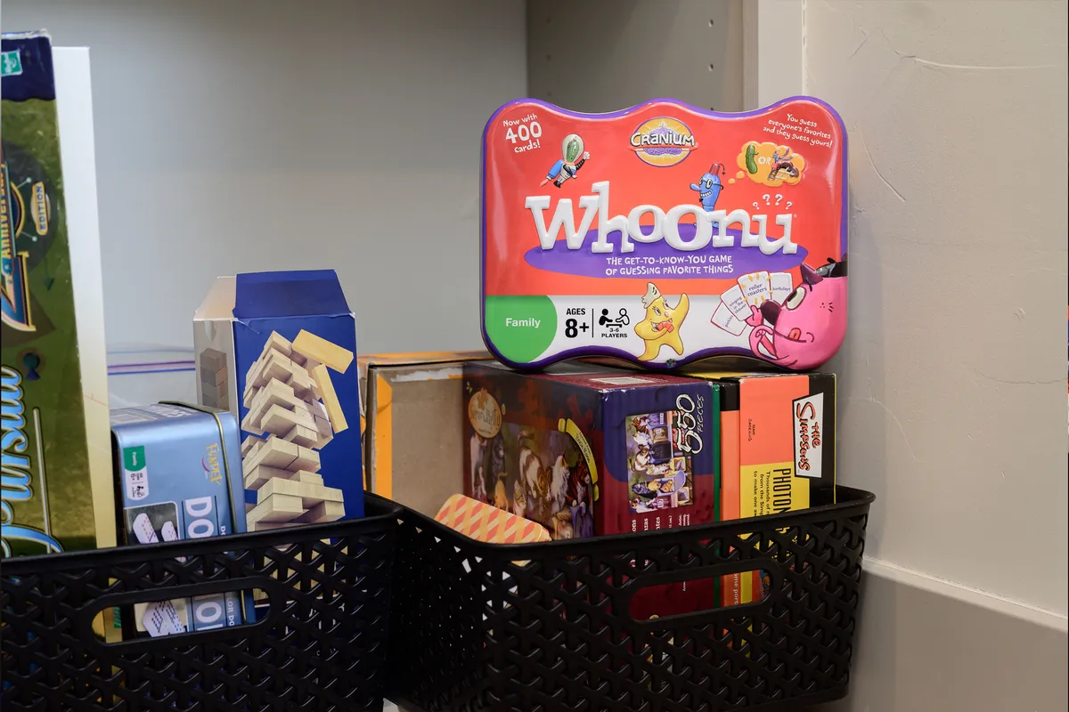 A collection of board games, including the 'Whoonu' box and black storage baskets, suggests a playful, social atmosphere. The games are attractively arranged, inviting families and friends to gather and make memories indoors.