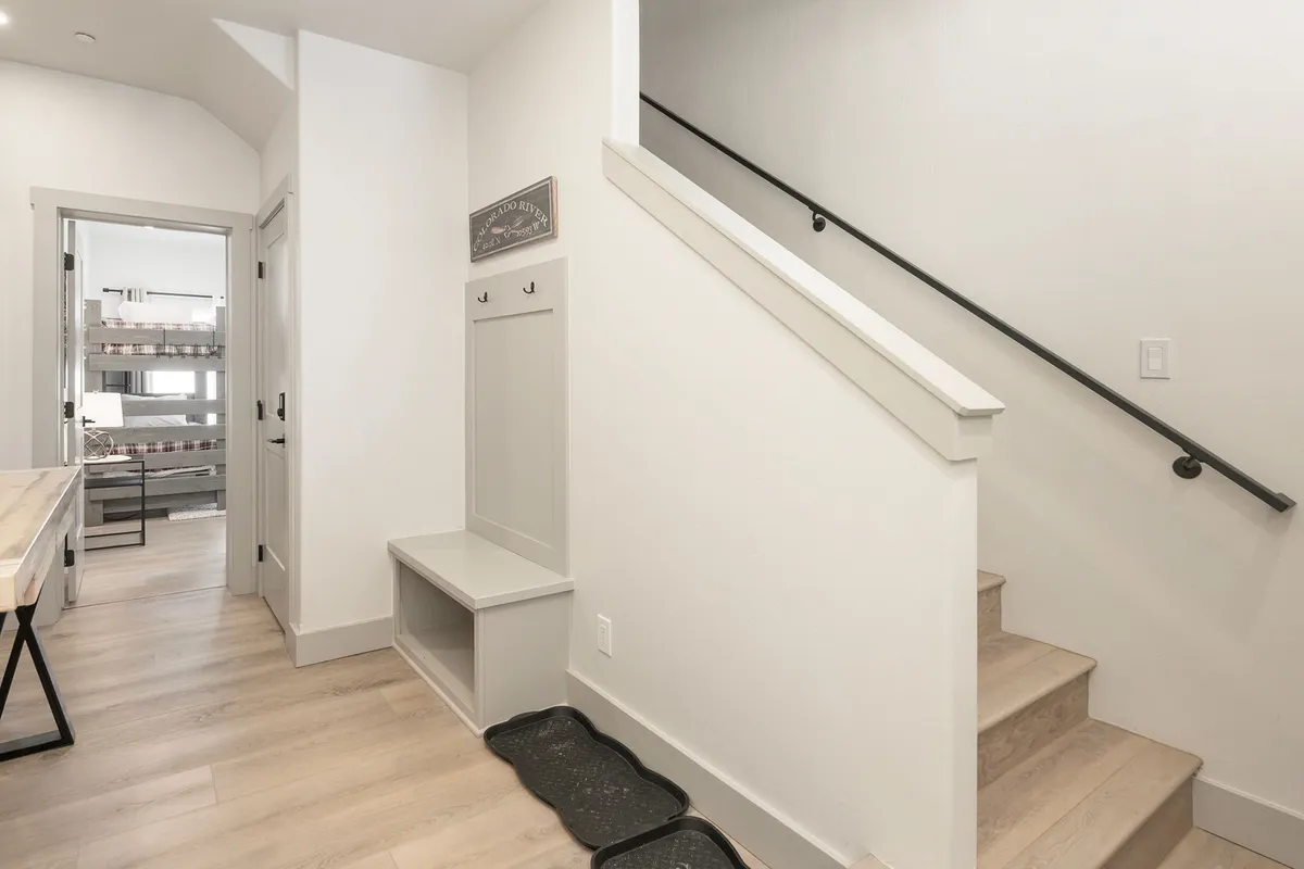 This image captures a welcoming ground-level entryway, featuring a staircase, a practical bench for removing shoes, and storage areas for personal items. The setup suggests a space designed for greeting guests and transitioning from outside to inside, with an inviting and organized atmosphere.